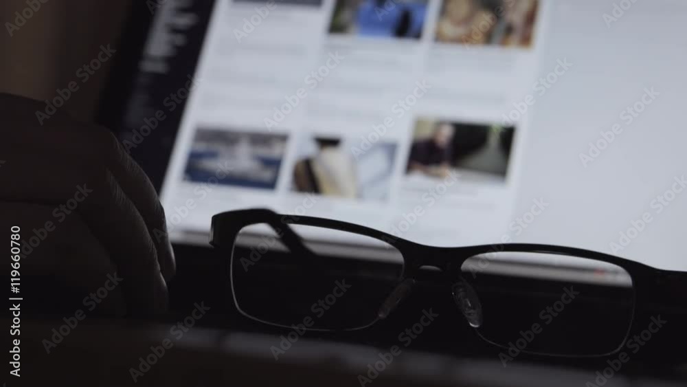 Human hand is scrolling a web site in the night. A glasses is near
