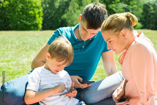 Family Using Smartphone In The Park © Andrey Popov