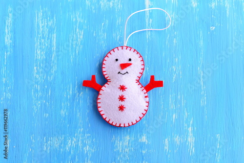 Fun felt Christmas snowman ornament isolated on a blue wooden background. How to make a Christmas snowman ornament. Step. Christmas tree decor idea for chilfren. Easy felt sewing crafts. Top view photo