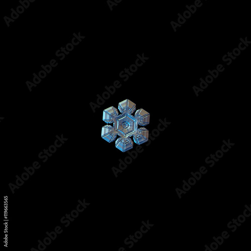 Snowflake isolated on black background. This is macro photo of real snow crystal: simple plate with relief and glossy surface.