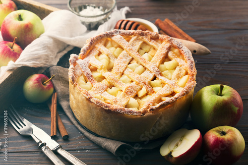 Homemade pie with apples, cinnamon and cream on dark rustic wooden background, selective focus. Toned effect