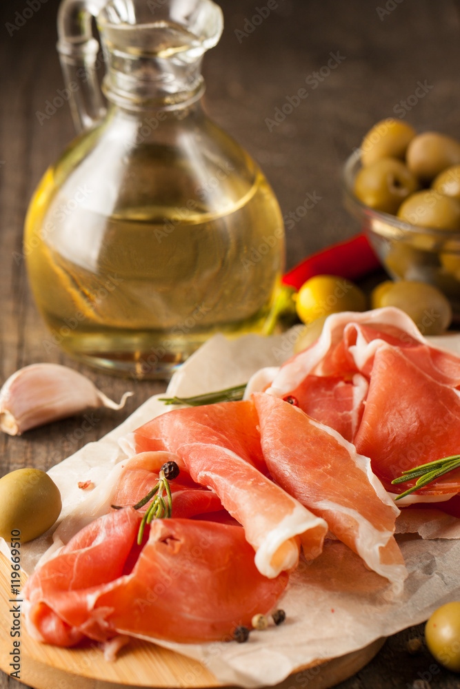 closeup of thin slices of prosciutto, jamon and ham with mixed olives and paprika on wooden cutting board