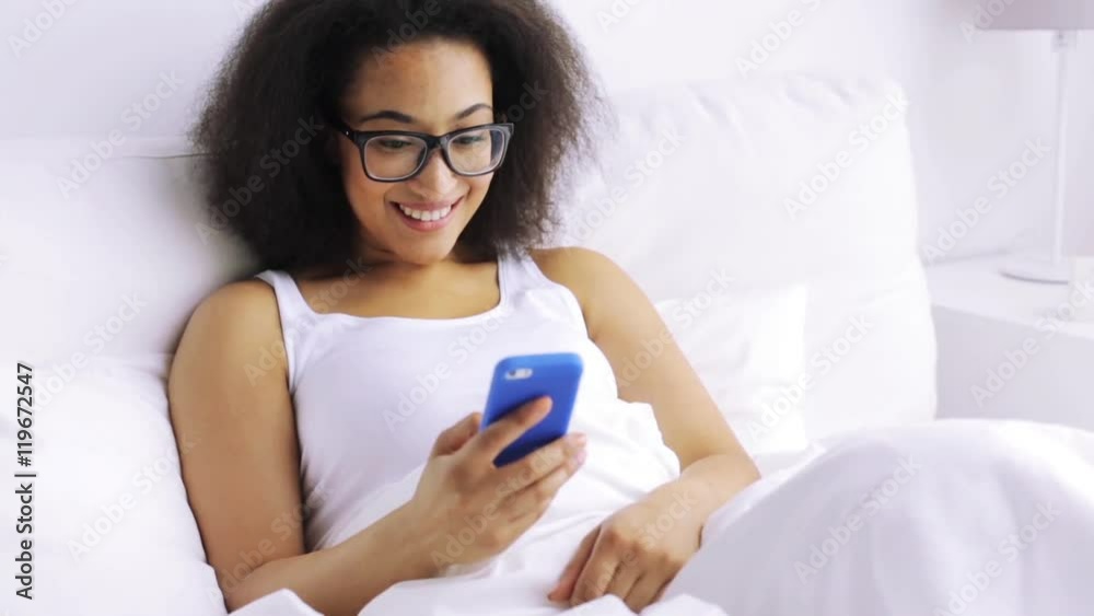 african woman with smartphone in bed at home african woman with smartphone in bed at home