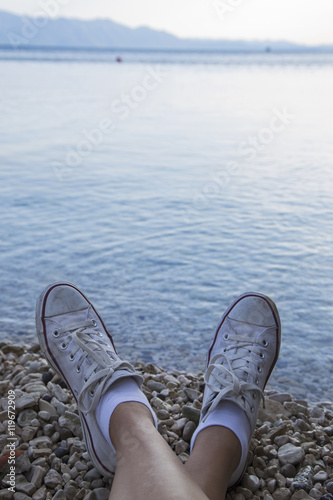 Female feet in sneakers on the background of a sea