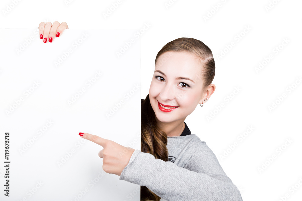 Smiling happy young woman standing behind and leaning on a white blank billboard or placard, expresses different