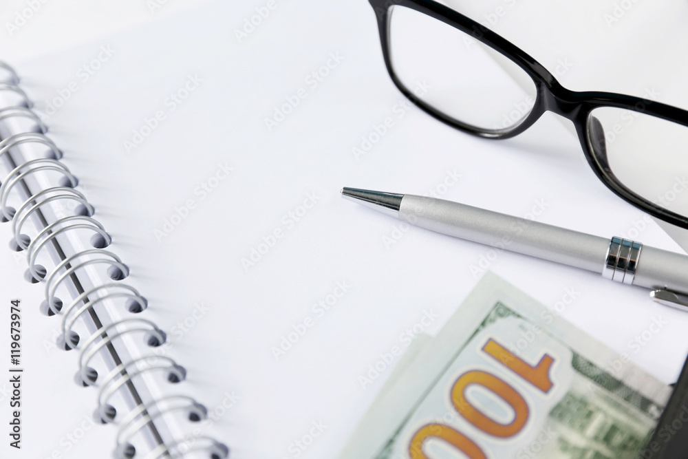 White blank notebook with silver pen and glasses. Some money and wallet are located close to it. 