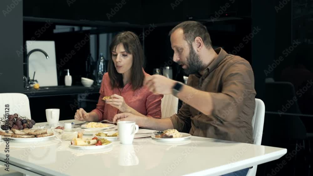 Young couple talking and eating breakfast by table at home
Young couple talking and eating breakfast by table at home
