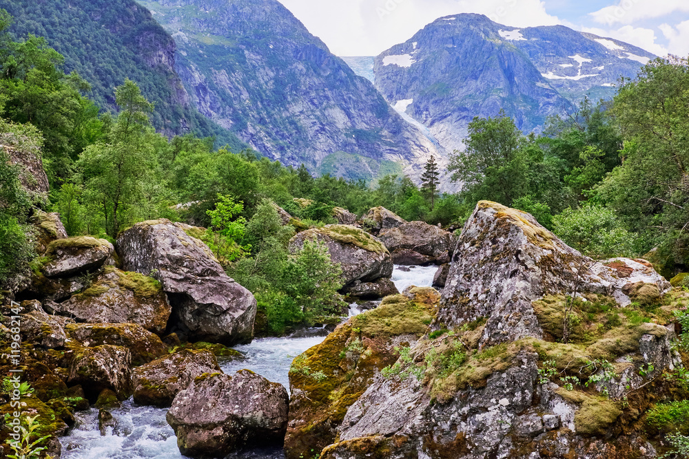 Norwegian landscape with gushing water in Bondhuselva running between giant rocks with thick moss vegetation, Folgefonna glacier is seen in the background