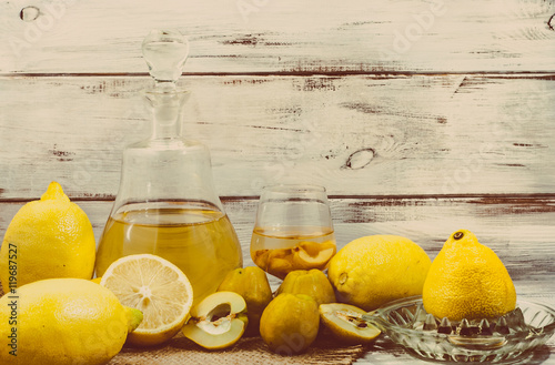 Fruit liquor in a glass bottle on rustic wooden table. Homemade alcohol made from fruit of lemon and quince