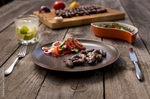"Churrasco de curacao",traditional Brazilian barbecue, grilled chicken hearts composition with tomatoes and onion salad an old wooden table.
