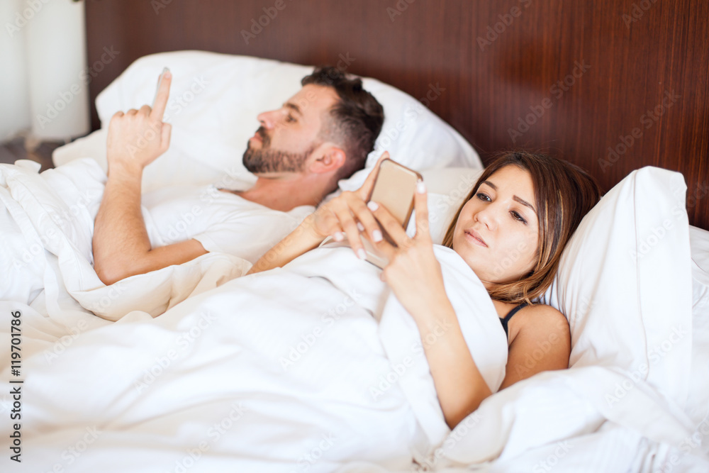 Couple texting on their phones in bed Couple texting on their phones in bed