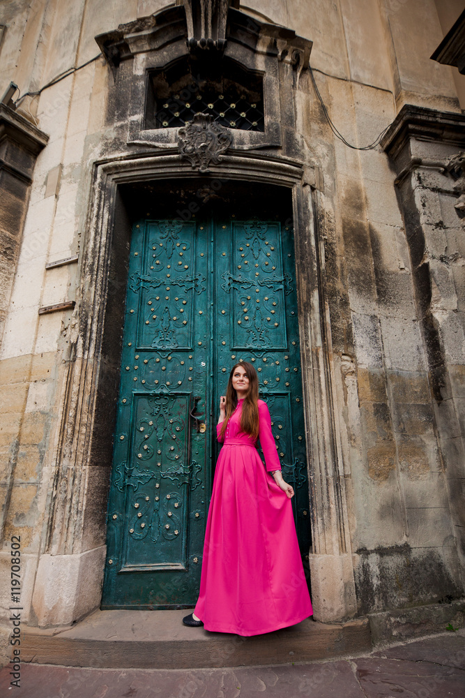 Amazing girl in pink dress is standing near doors