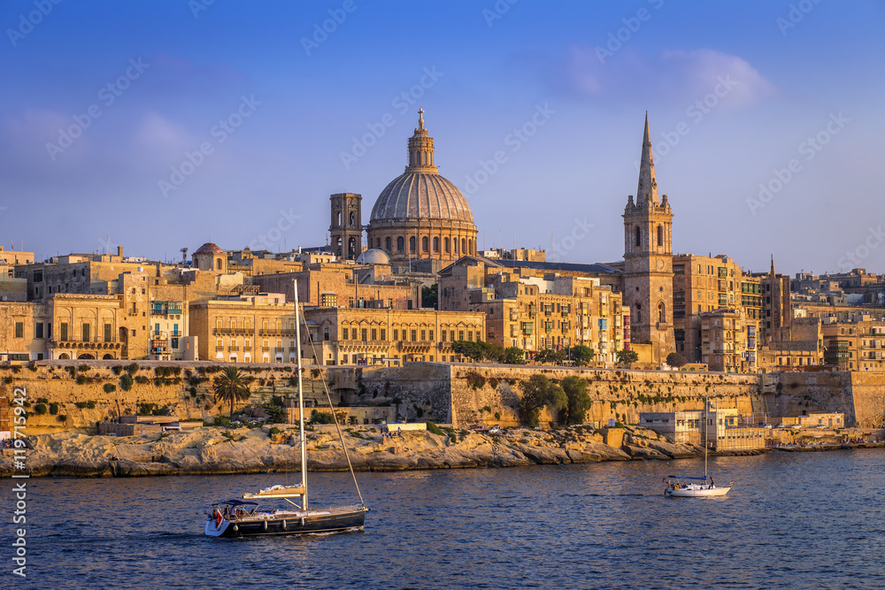 Valletta, Malta - Sailboats and the famous St.Paul's Cathedral with the walls of Valletta at sunset