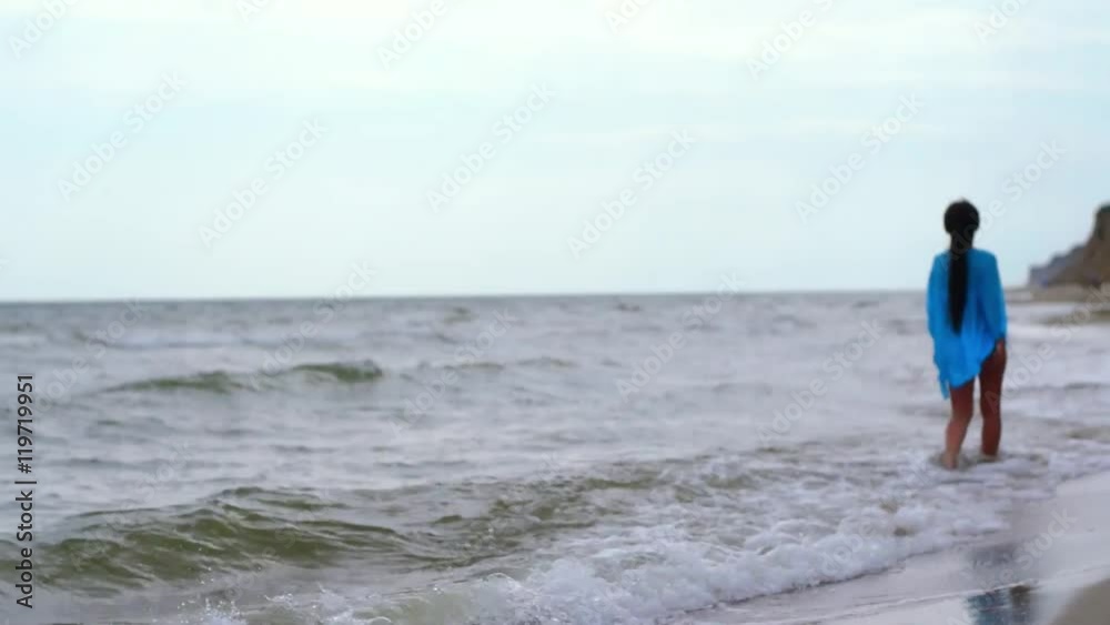 Girl in a blue cape walks on the sandy seashore Girl in a blue cape walks on the sandy seashore