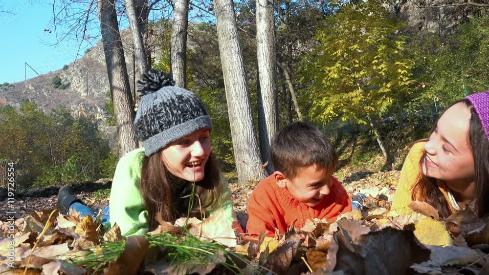 Two girls and a little handsome boy lying on fall leaves in park, dolly shot Two girls and a little handsome boy lying on fall leaves in park, dolly shot