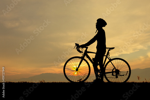 Silhouette of man, him standing with bicycle and looking at the sky in sunset time.