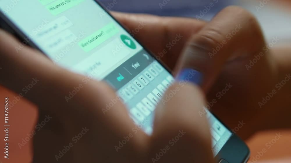 Young woman using smartphone while doing homework. Hispanic people and college education. Female student studying and texting with mobile telephone at home, typing text message on cell phone. Close-up