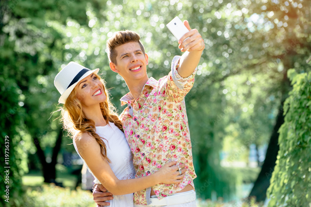 Naklejka premium Youth and technology. Young smiling loving couple taking selfie in park