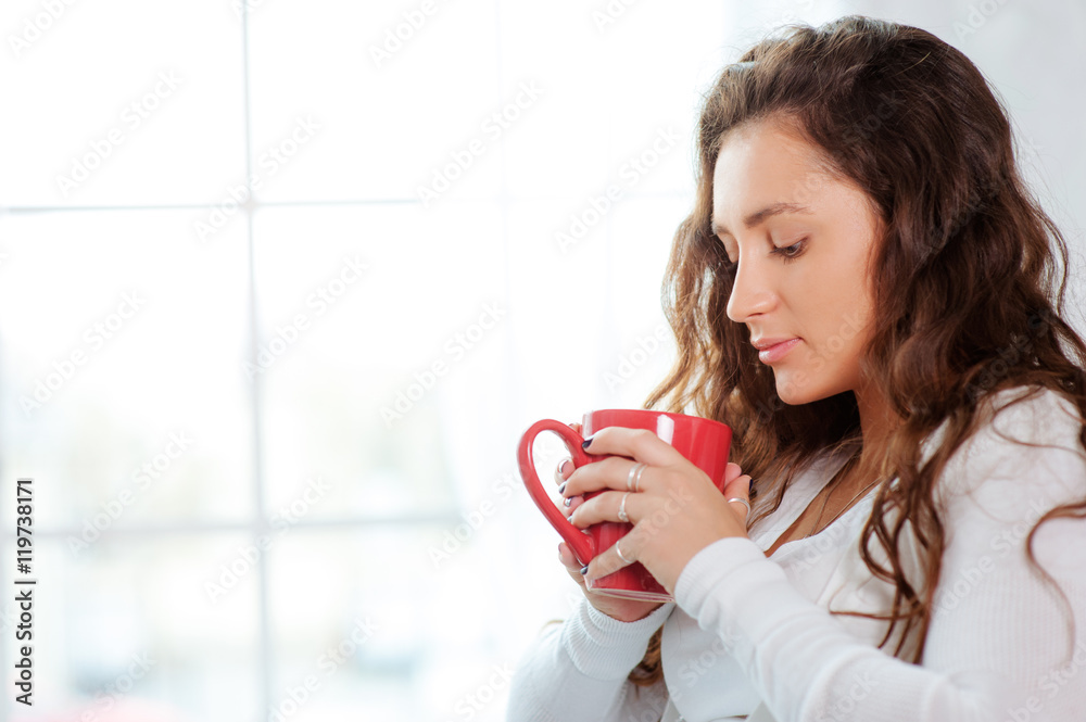 Calm and coziness. Beautiful young woman with cup of tea sitting against the window at home Calm and coziness. Beautiful young woman with cup of tea sitting against the window at home