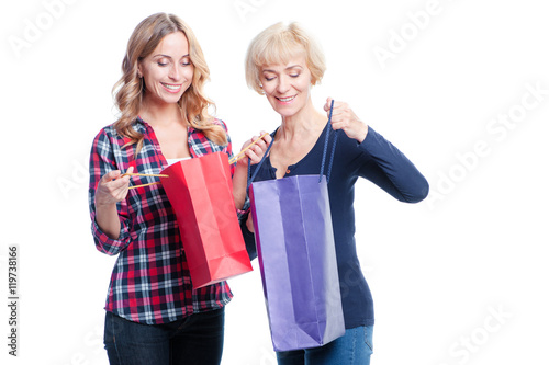 Shopping with mom. Pretty happy senior woman with her smiling adult daughter holding paper bags. Isolated on white.