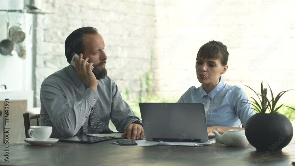 Businesspeople with cellphone, laptop and tablet working by table in open kitchen at home
