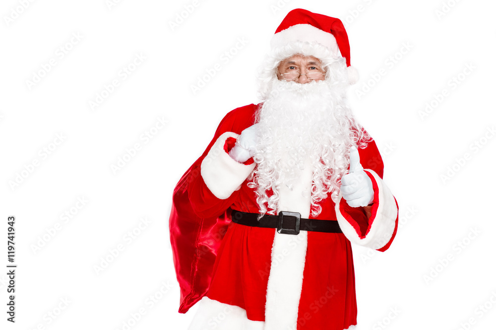 Traditional Santa Claus showing his thumb up and carrying sack with presents on white background
Traditional Santa Claus showing his thumb up and carrying sack with presents on white background