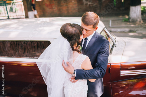 Happy bride and groom hugging and posing near old retro car limousine before wedding ceremony © nataliakabliuk