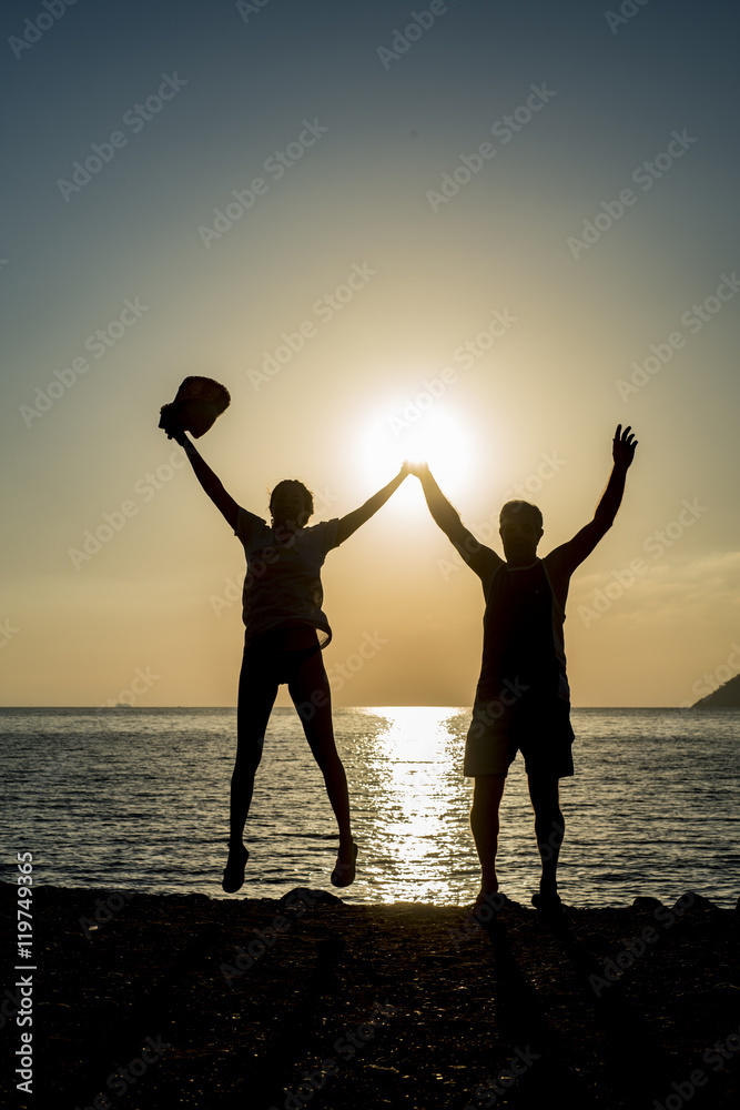 Fototapeta premium Silhouette Beautiful couple are having fun jumping on the water sunset horizon 