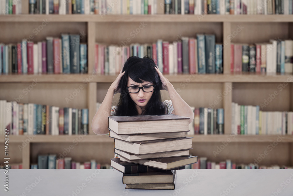 Attractive female student stress looking at books in library Attractive female student stress looking at books in library