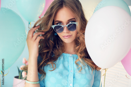 fashion interior photo of beautiful young girl with dark curly hair and tender makeup, posing with colorful air balloons 