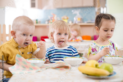 three children eating from plates in day care centre