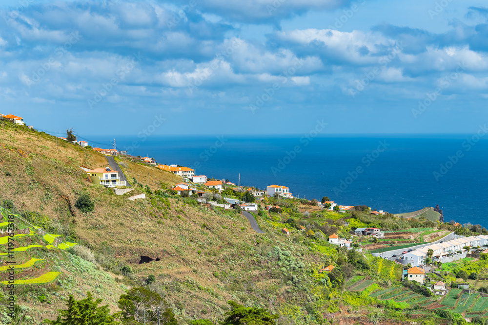 View of Atlantic Ocean rocky volcanic hill on Portuguese Madeira. 
Landscape dotted with tropical foliage and Mediterranean style buildings on a bright summer day, image for travel business concept