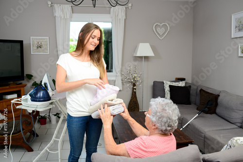cheerful young girl ironing and helping with household chores an elderly woman at home