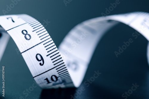 White measuring tape on a dark background. Rolled tape with numbers