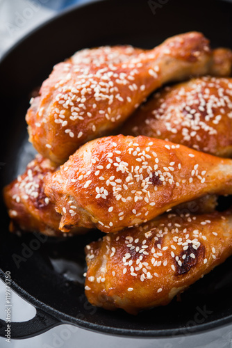 Baked spicy chicken legs with sesame in cast iron frying pan on white background close up. Asian food.