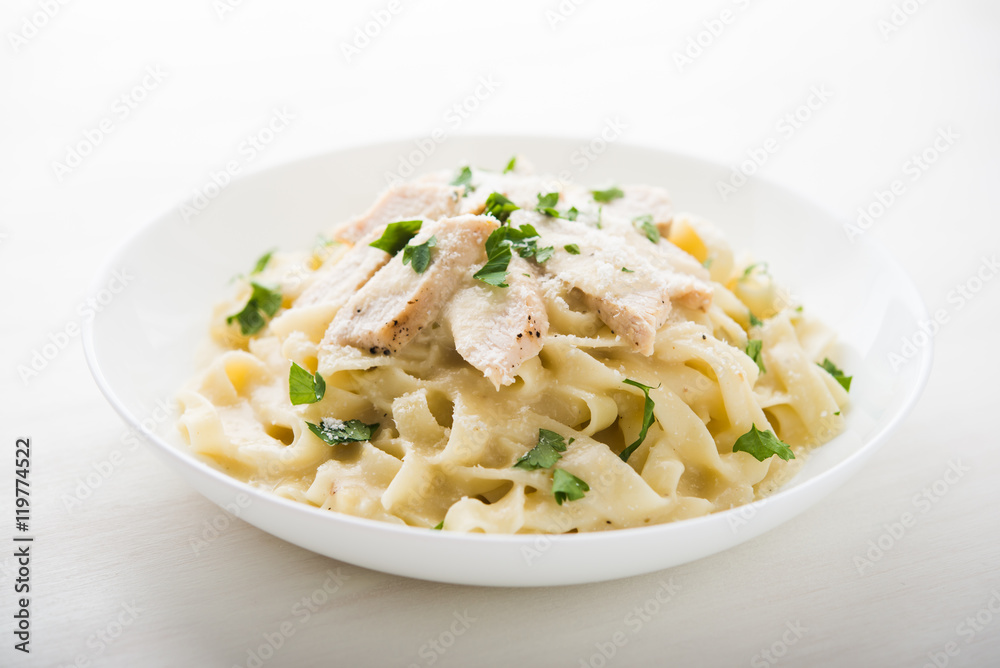 Pasta fettuccine alfredo with chicken, parmesan and parsley on white background close up. Italian cuisine.