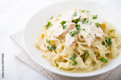 Pasta fettuccine alfredo with chicken, parmesan and parsley on white background close up. Italian cuisine.