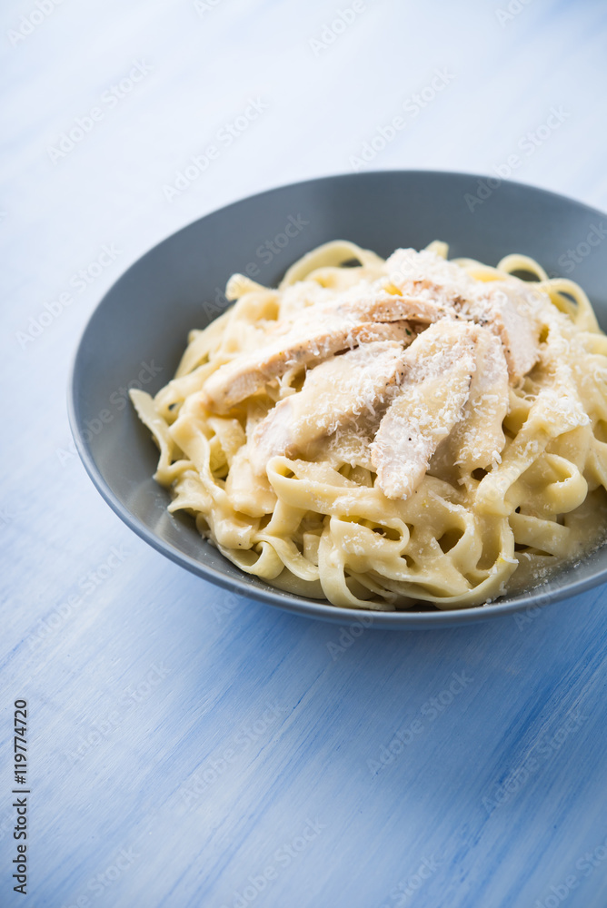 Pasta fettuccine alfredo with chicken and parmesan on blue wooden background close up. Italian cuisine.