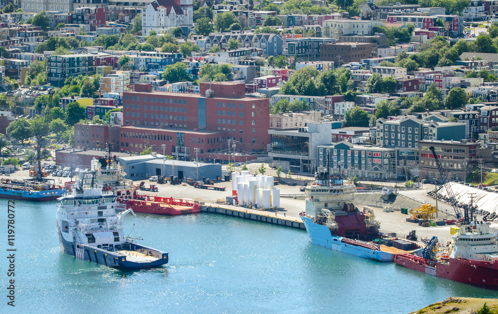 Commerce, trade, cargo and ships of all kinds lined up along St John's Harbour in Newfoundland Canada.  Boats slowly move about amongst those docked in harbour.