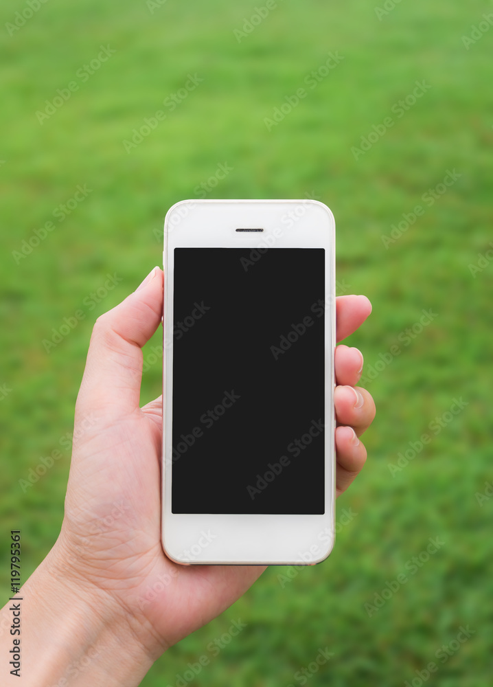 Human hand holding mobile phone against blurred green field background, Vertica