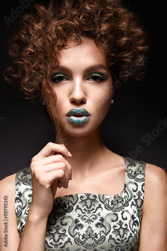 Beautiful girl with curls and green glitter on the eyelids and lips. Model woman with beautiful makeup and curly hairstyle. Beauty face. The photo was taken in a studio.