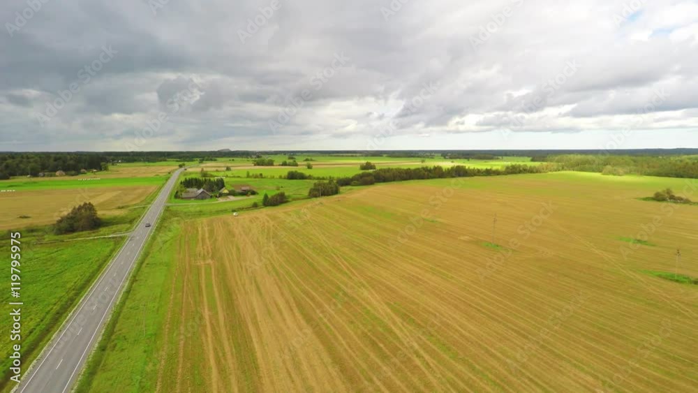 Aerial shot with a cars passing driving to the horizon. Green fields and massive clouds. Summer landscape. Aerial shot with a cars passing driving to the horizon. Green fields and massive clouds. Summer landscape.