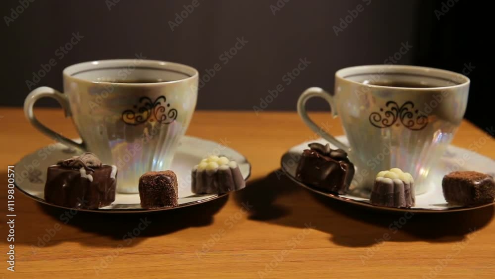 Chocolate candies and tea set on a wooden table.Cup of hot blak tea with chocolate candy.Porcelain tea set on an black background.Two teacups and teapot.Vintage tea set for two persons. Chocolate candies and tea set on a wooden table.Cup of hot blak tea with chocolate candy.Porcelain tea set on an black background.Two teacups and teapot.Vintage tea set for two persons.
