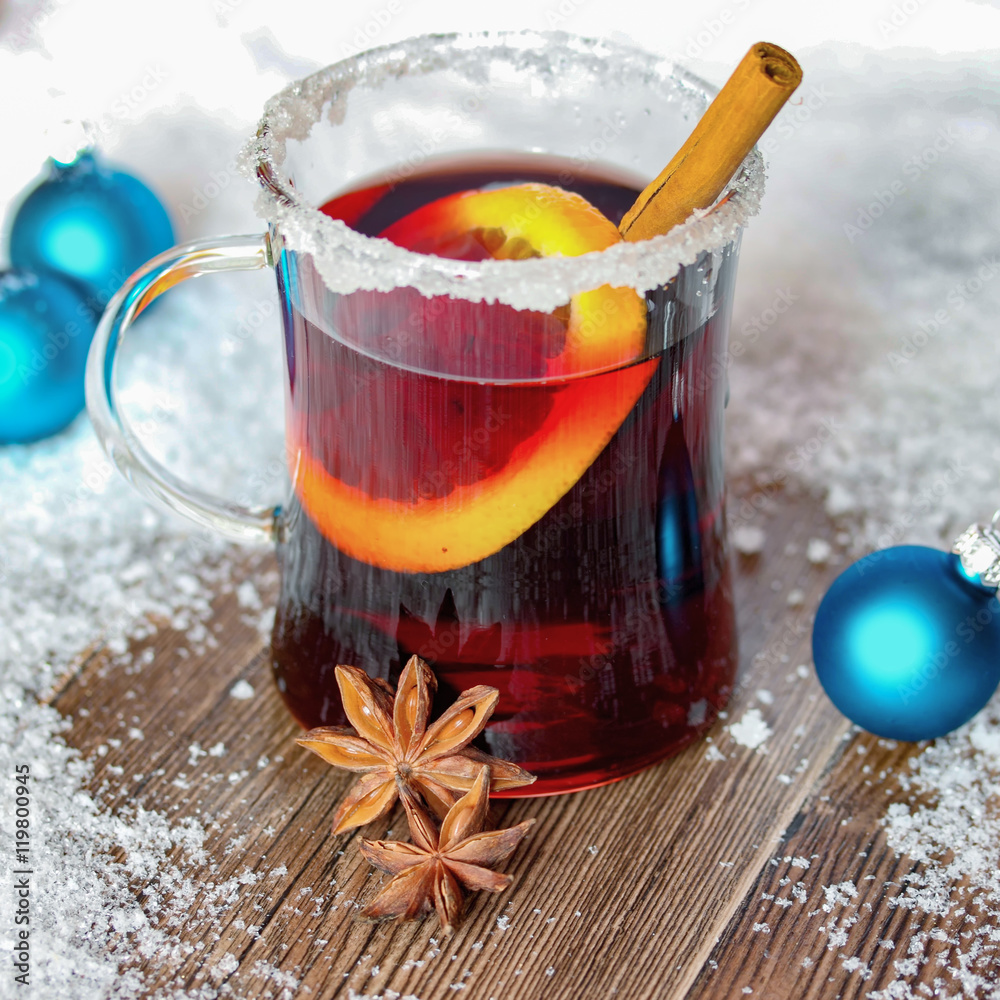 Fototapeta premium Ein Glas mit Glühwein, Orgenscheibe, Zimtstange auf altem Holz mit Schnee - Weihnachten