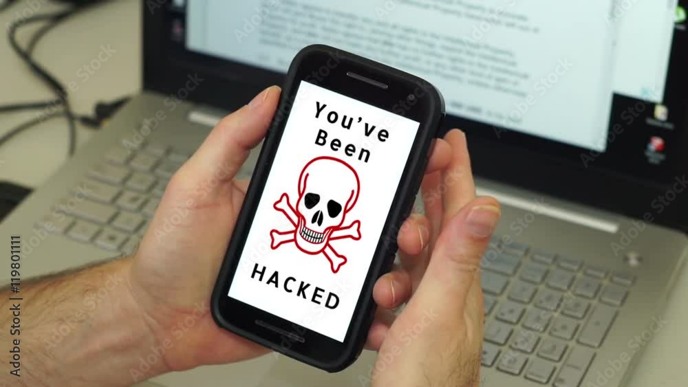Anonymous man holds his mobile phone with a skull and crossbones flickering on the screen telling him that his phone has been hacked.
