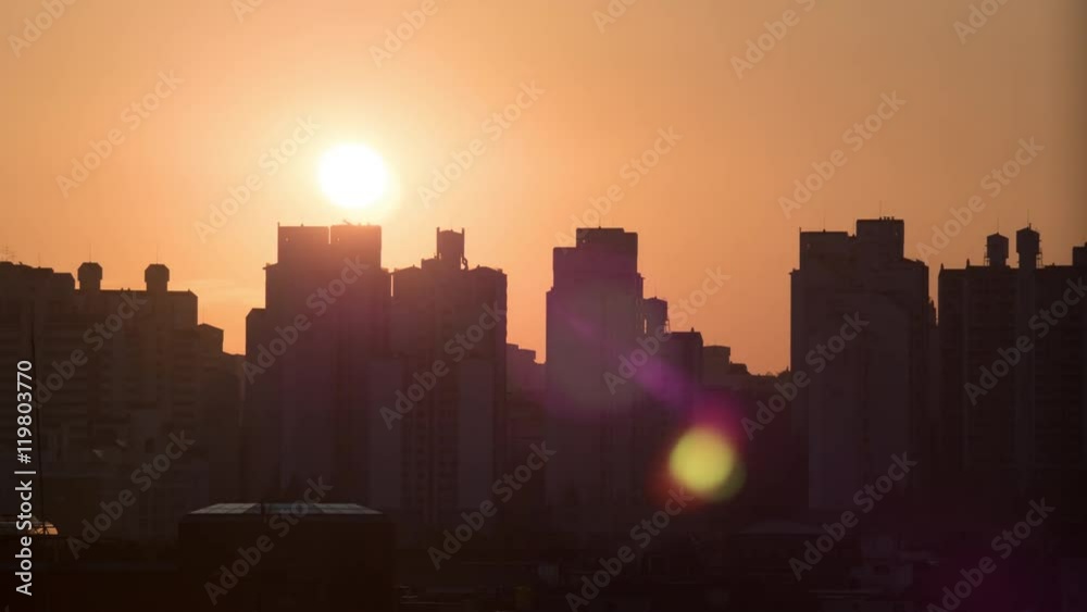 Time lapse shot of sun rising and moving in the sky, city modern buildings silhouettes on the foreground in red color. Seoul, South Korea