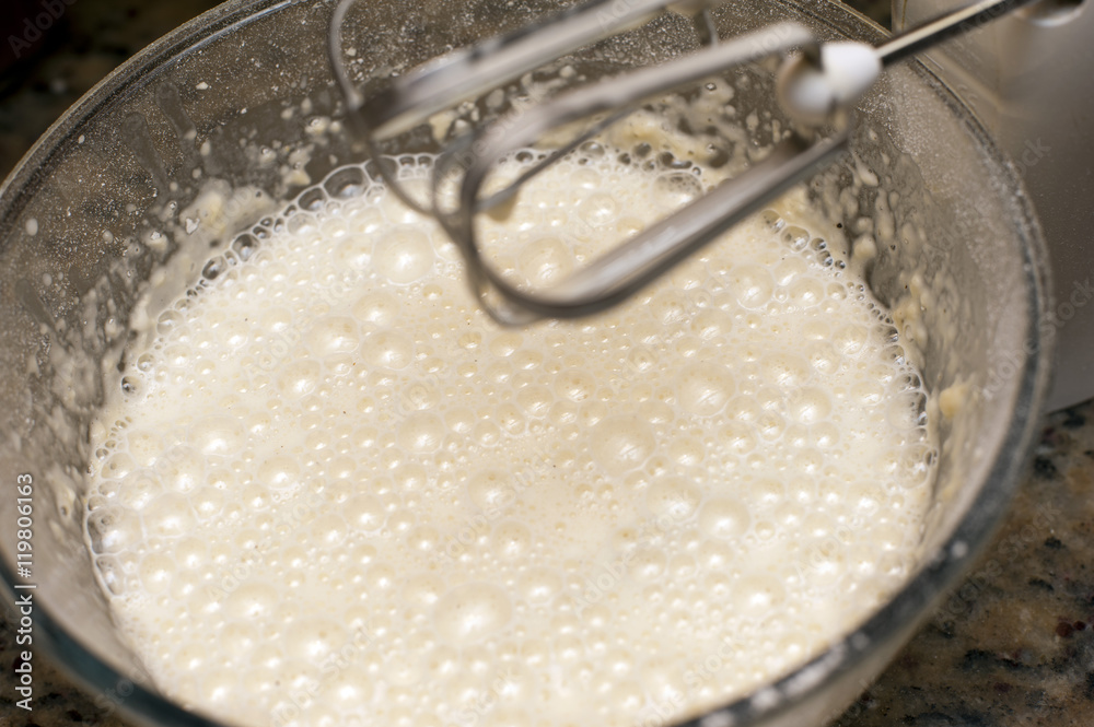 Frothy white liquid in glass mixing bowl Frothy white liquid in glass mixing bowl