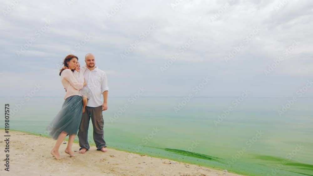 Young family of three posing for a photograph in the background of the sea Young family of three posing for a photograph in the background of the sea