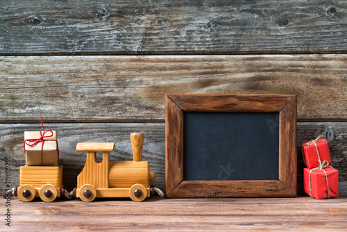 Merry Christmas decorations, empty chalkboard with toy wooden train and christmas gifts on a timber background