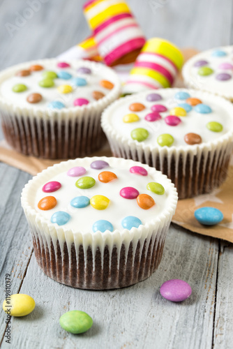 Chocolate cupcakes with white icing and colored smarties, wooden background